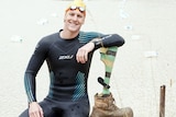 Col Pearse in a wetsuit and swimming cap sits on the banks of a large dam with makeshift laneropes.