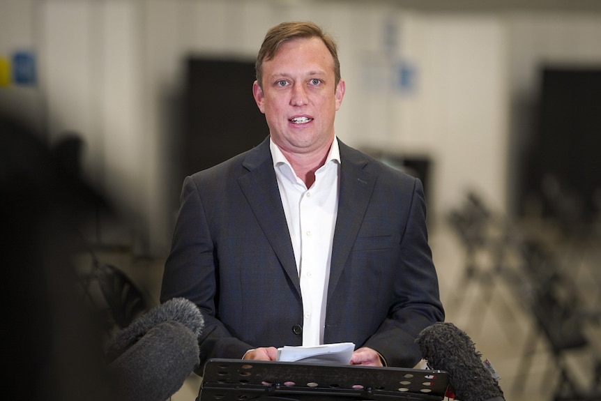 Steve Miles in a black blazer, white shirt, speaks into microphones at a lectern.