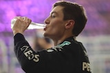 George Russell takes a swig out of a bottle of water. Purple lights fill the background