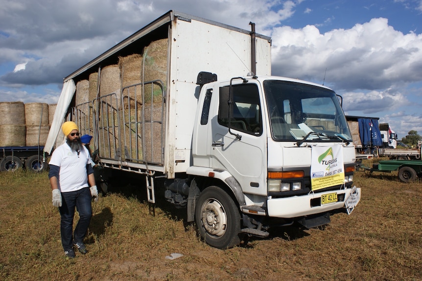 Amar walks in front of a large truck filled with hay, wearing gloves.
