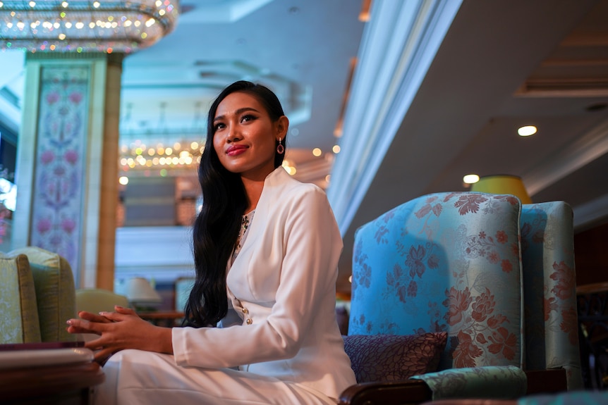 Una glamorosa mujer asiática de pelo largo y pantalones blancos sonríe en un hotel decorado.