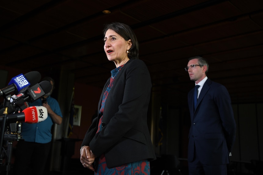 Gladys Berejiklian speaks into microphines while Dominic Perrottet stands behind her.
