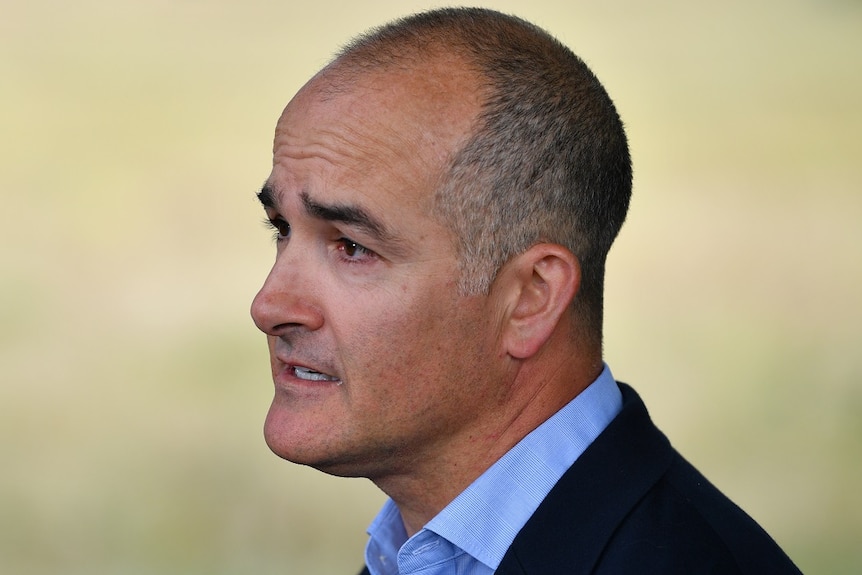 James Merlino, wearing a blue shirt and black jacket, speaks at an outdoors press conference.