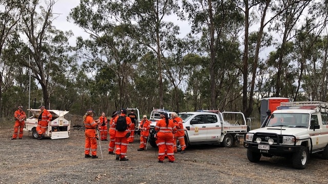 SES officers gather around cars in bushland, about to commence a search.