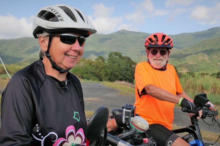 Female and male cyclist, both with white hair, smiling on their bikes.