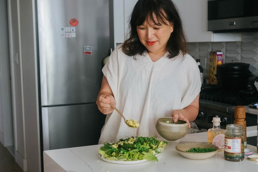 Hetty Lui McKinnon serving sauce gribiche onto a crunchy green salad in a modern kitchen.