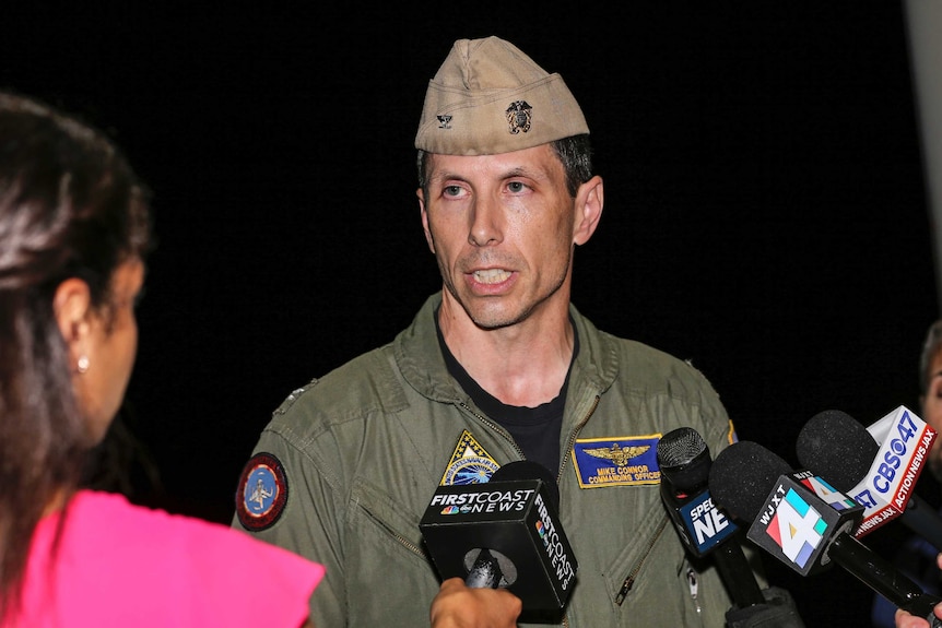 A man wearing a military uniform talks to news reporters.
