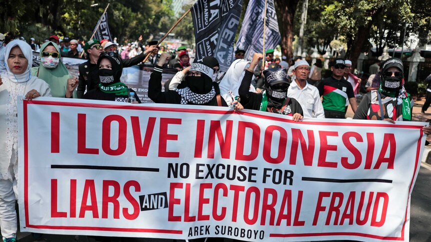 Protesters display a banner saying I love Indonesia as they march down the street with flags.