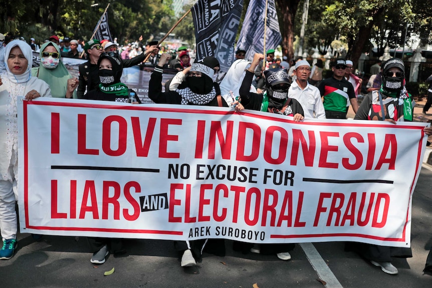 Protesters display a banner saying I love Indonesia as they march down the street with flags.