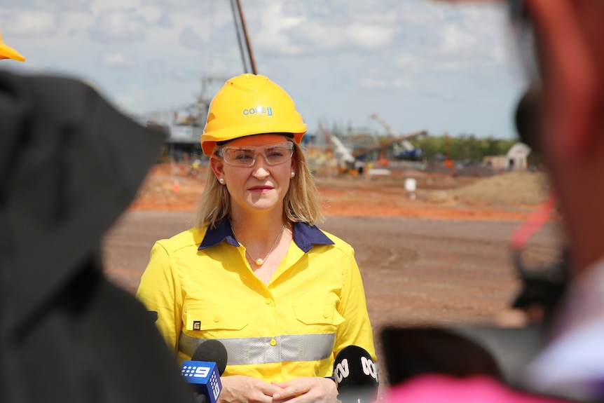 A blonde woman wearing a hard hat, high-vis jacket and safety glasses in front of a mine