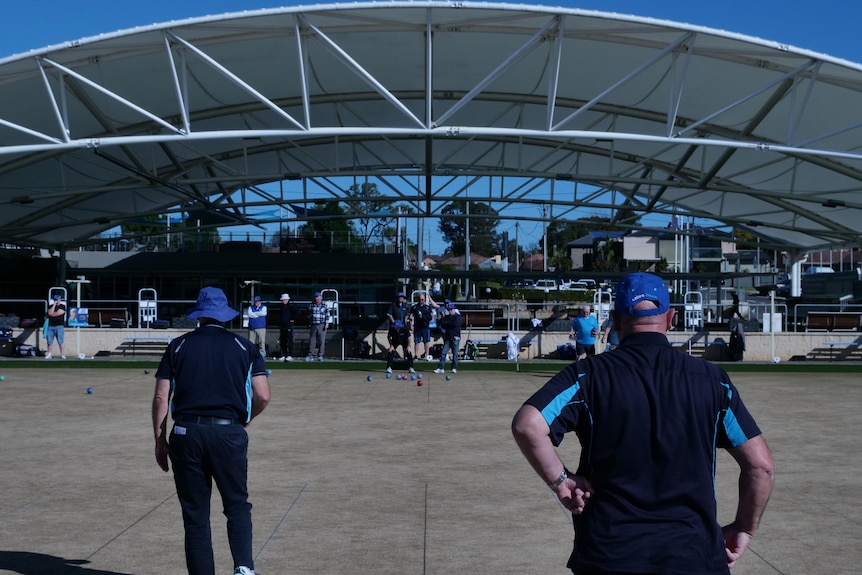 Men playing lawn bowls in front of a shelter structure