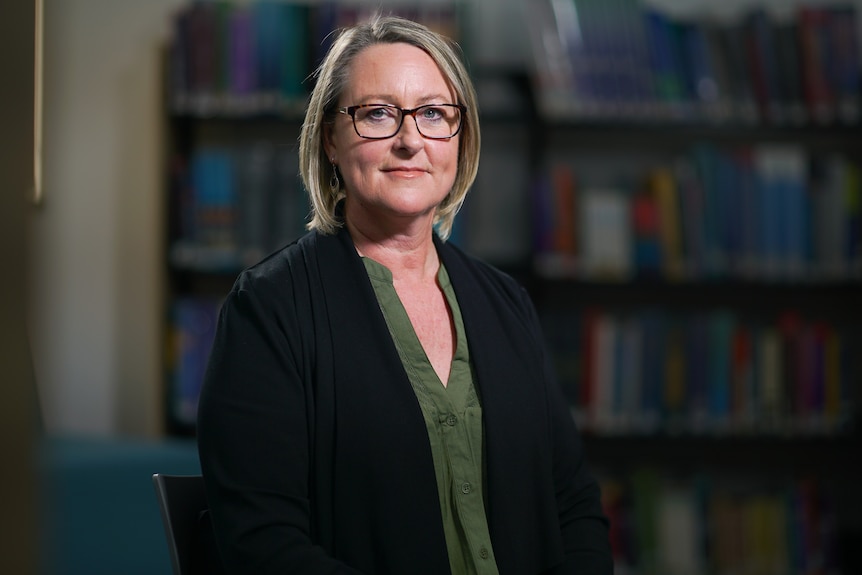 A woman wearing a black jacket and green shirt in a room with books