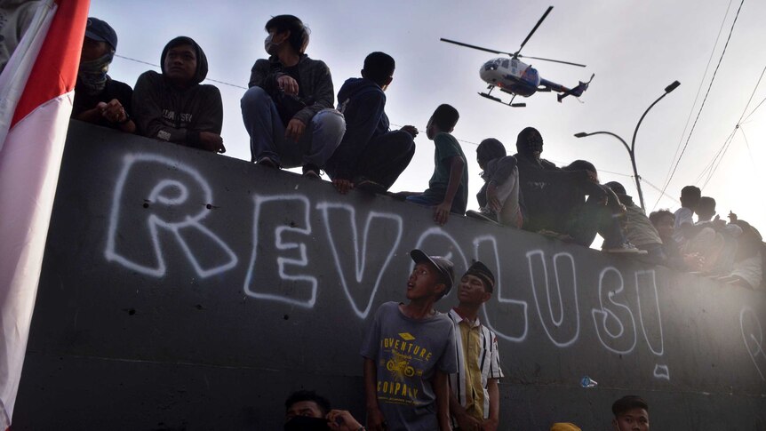 A police helicopter flies past as student protesters look on during a rally in Makassar, Indonesia.