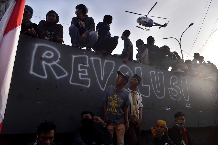 A police helicopter flies past as student protesters look on during a rally in Makassar, Indonesia.