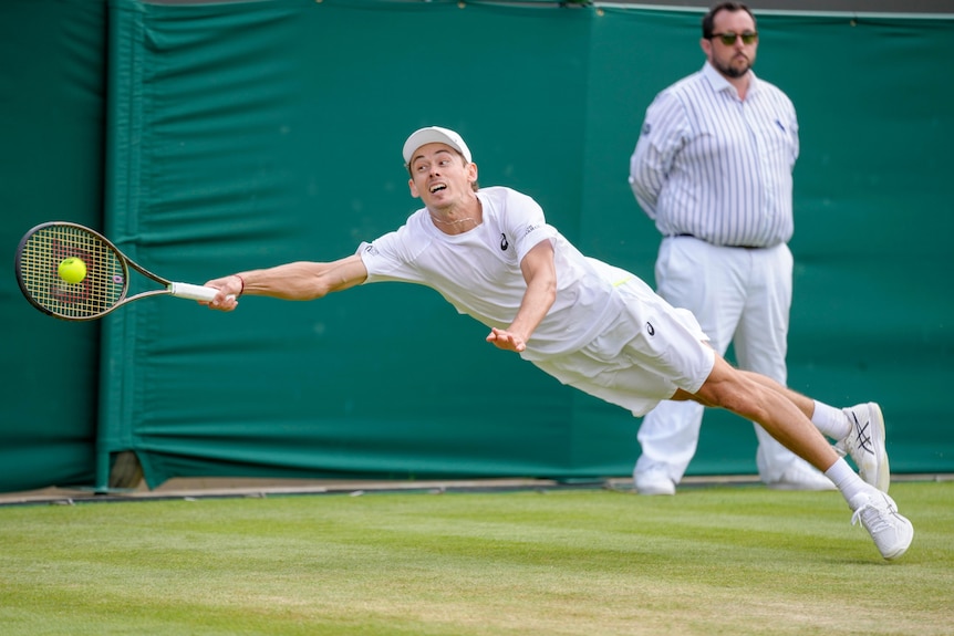 El tenista australiano Alex de Minaur se lanza para jugar un golpe de derecha en Wimbledon.
