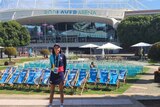 A young girl stands before a lawn covered in chairs before a large sports arena