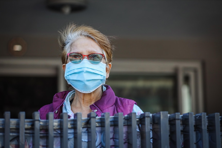 A woman wearing a face mask look over a fence. 
