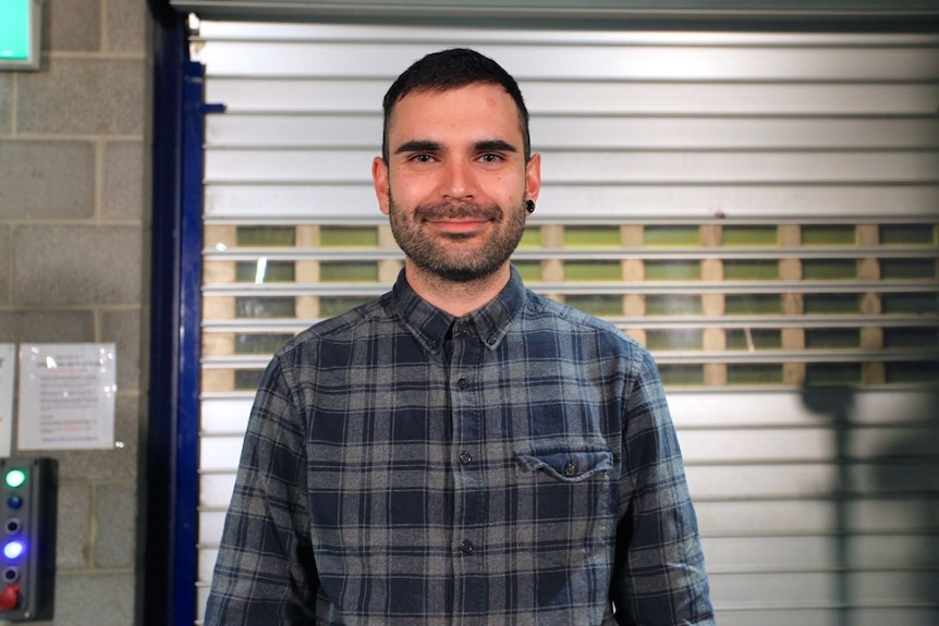 Kyle Tinnion standing in front of a metal roller door in a checked shirt.