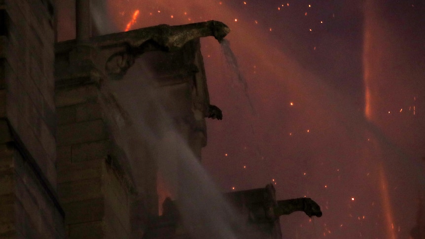 Fire behind silhouetted gargoyles as water jets from the fire brigade look to extinguish flames at night