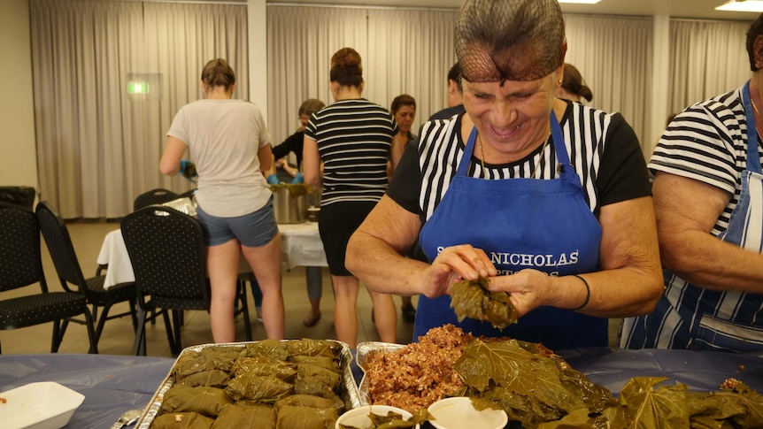 older woman laughing as she makes dolmade.