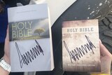 A woman holds two Holy Bibles, both bearing Donald Trump's signature.