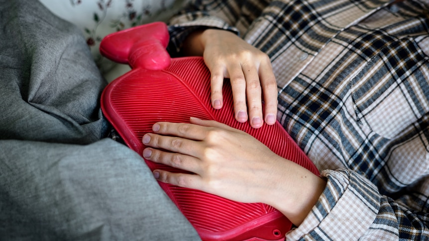 close up of woman holding hot water bottle on her stomach