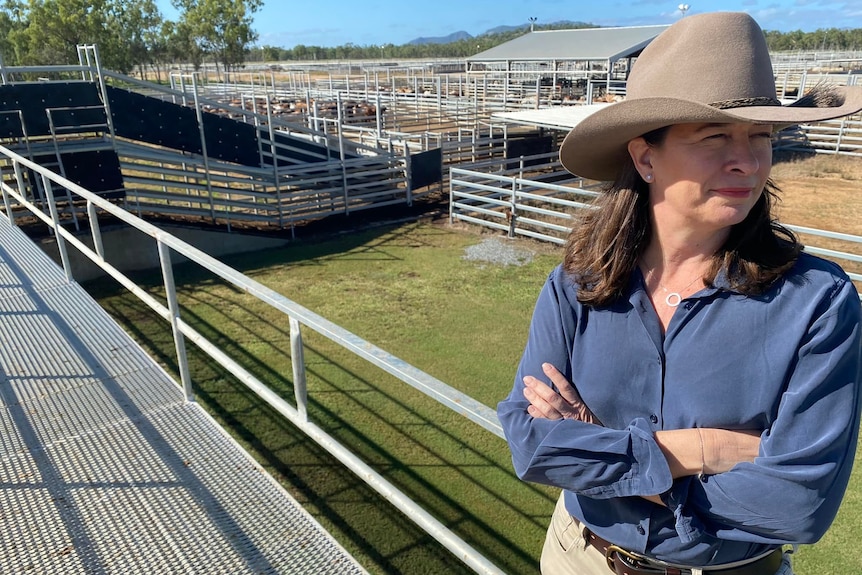 A woman in a blue shirt and cowboy hat sits near livestock gates