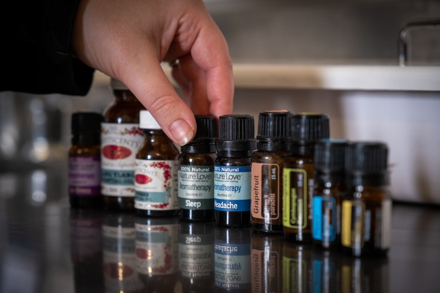 A line up of essential oils in glass bottles, a close up of a person's hand lifting one up
