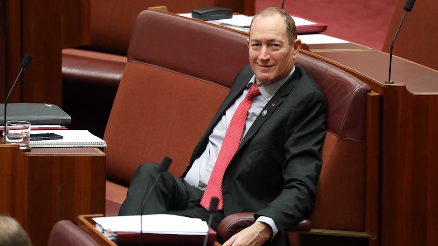 Anning is sitting in his seat, smiling as he looks towards the camera.