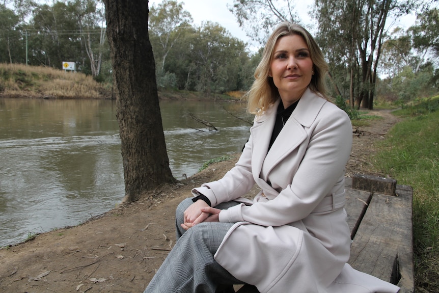 A woman sitting by a river, looking of into the distance