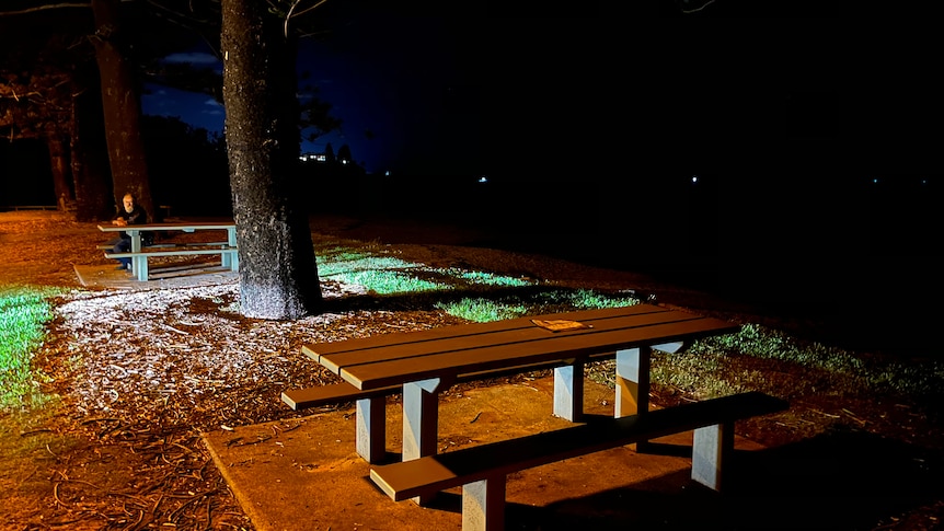 An empty wooden table soaked by rain and illuminated next to the darkness of the sea at night