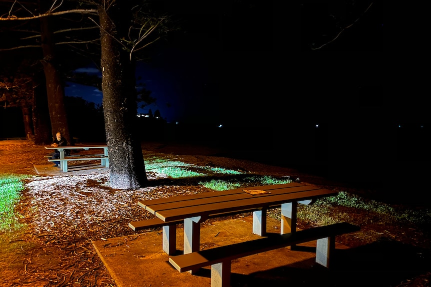 An empty wooden table soaked by rain and illuminated next to the darkness of the sea at night
