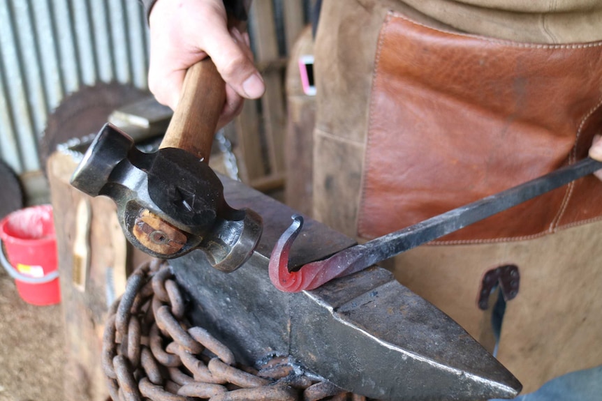 a hammer shapes a metal rod into a curve