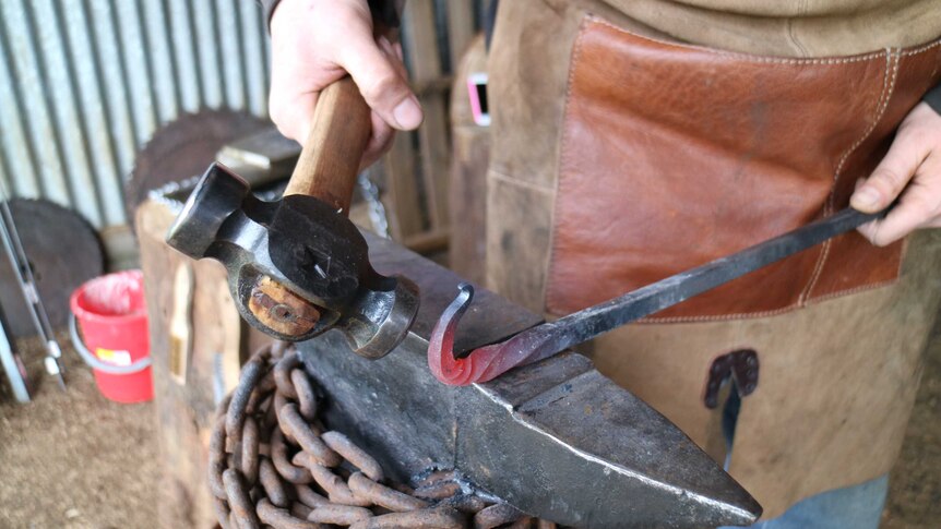 a hammer shapes a metal rod into a curve