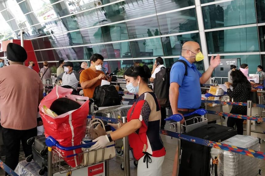 People waiting in a line with their bags for security at an airport.