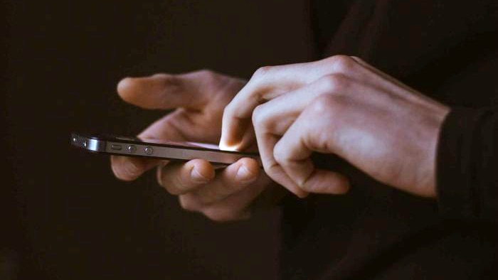 A man's hands, holding and using an iPhone.