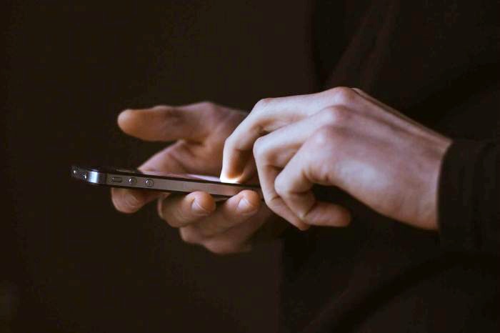 A man's hands, holding and using an iPhone.