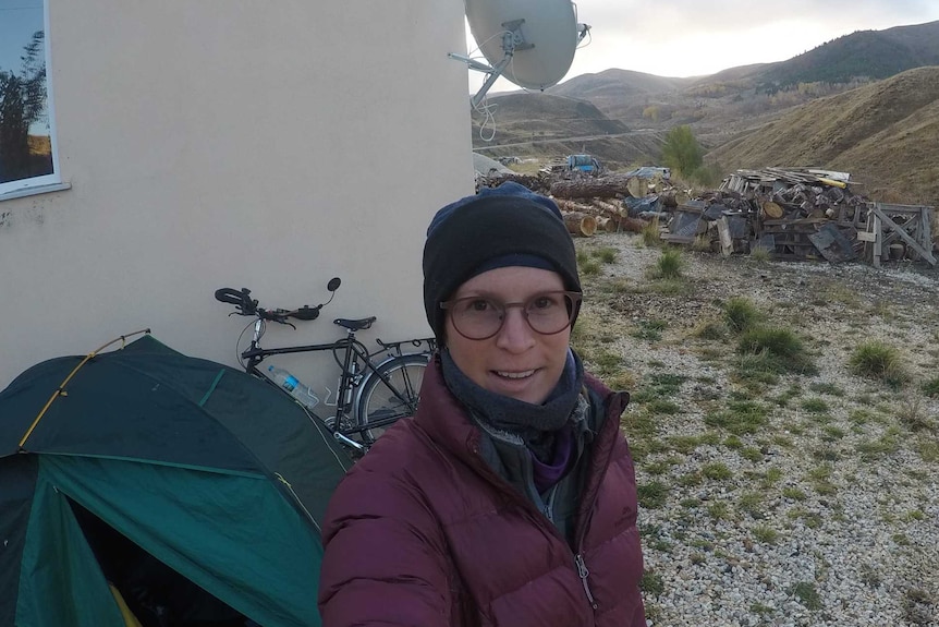 Lauren O'Bryan looks to the camera and slightly smiles. A rugged backdrop is seen in the distance, with a tent behind her.