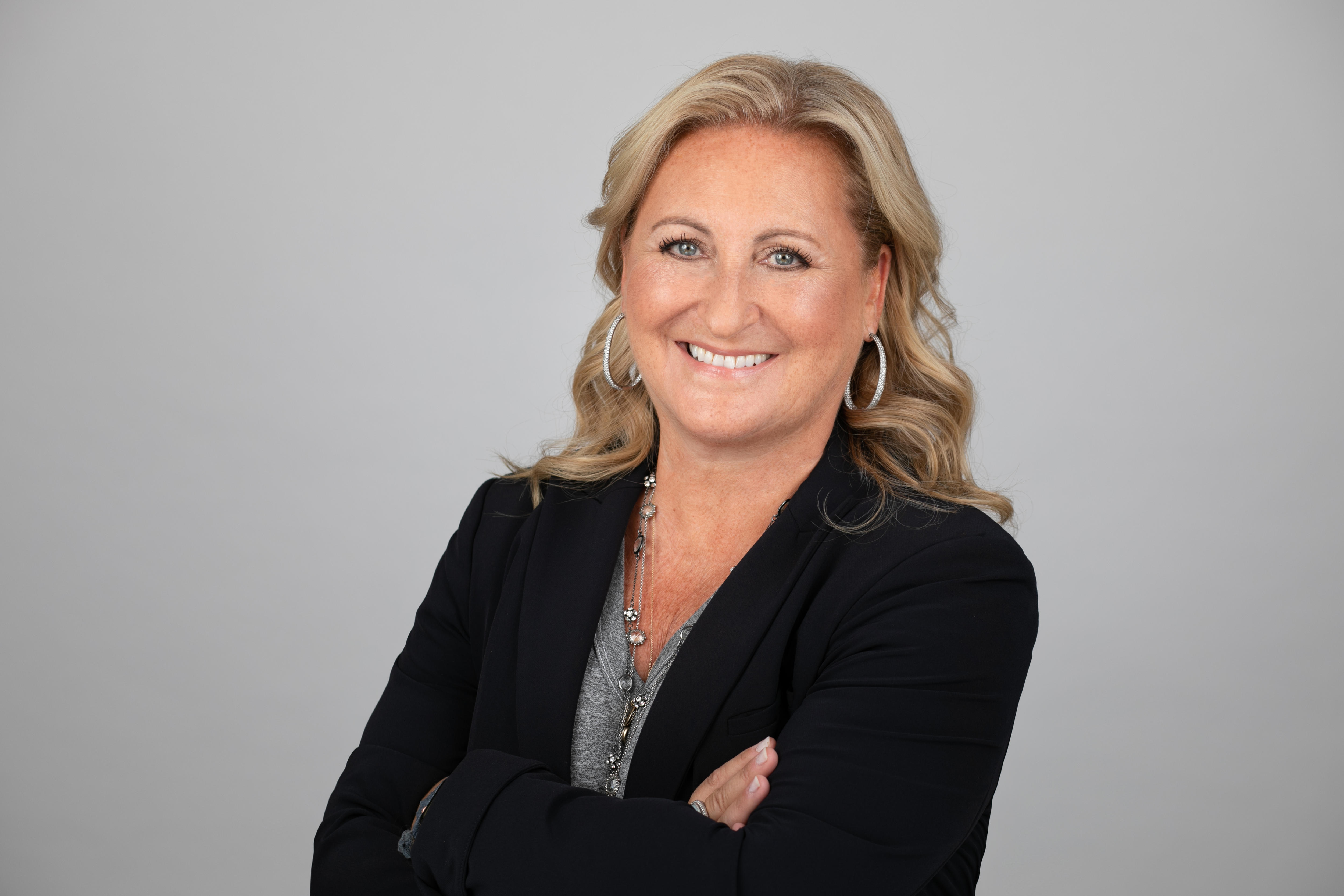 A professional headshot of a woman with blonde wavy hair.