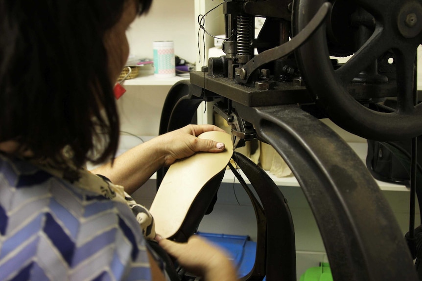 A woman sews leather on an old machine