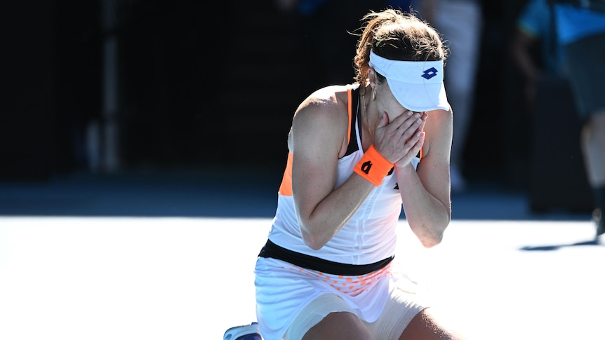 A French female tennis player kneels on the court with her face in her hands.