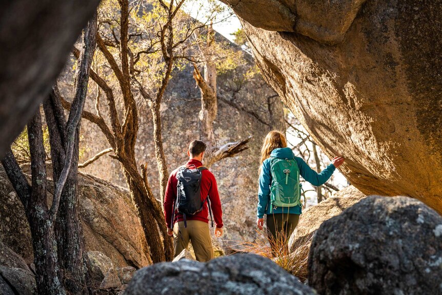 A man and woman are seen from inside a cave looking out onto the bush at sunset.