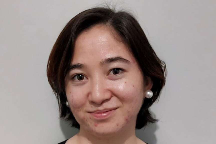 A young, smiling Afghan woman wearing pearl earrings and a black top