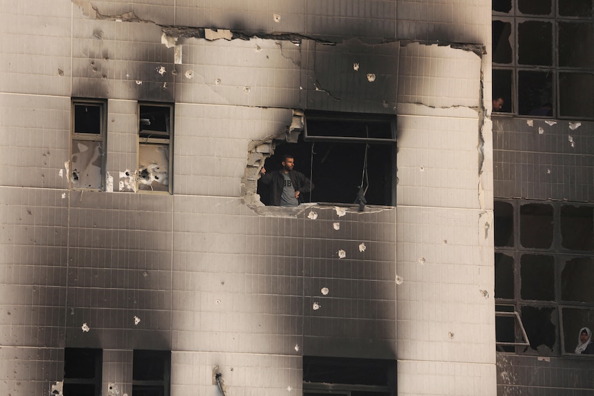 A man stands in the window of a charred building with bullet holes