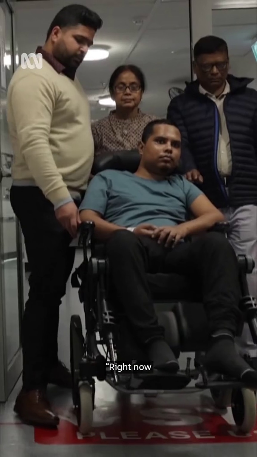 A man with brown skin sits in a wheelchair surrounded by three people with brown skin