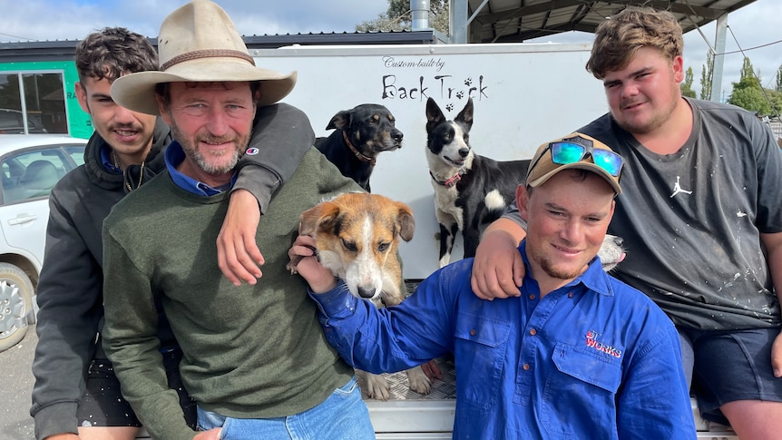 Four men, one wearing a cowboy hat and three dogs 