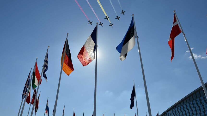 Fighter jets fly over flags representing the members of NATO.