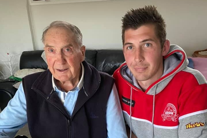 An elderly man and a young man pose for a photo.