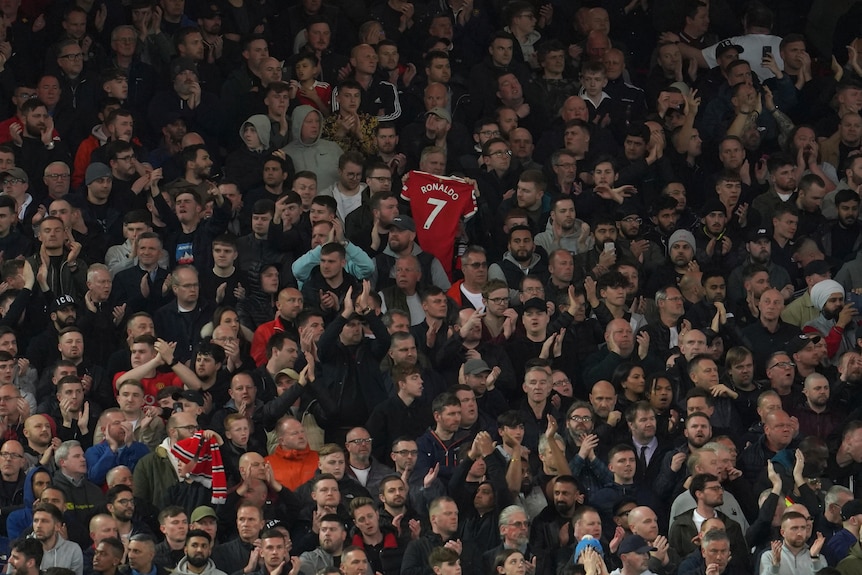 A man holds up a red Ronaldo 7 shirt in amongst a crowd of football supporters