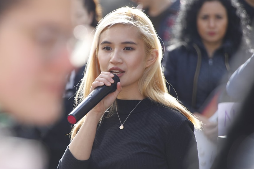 Belle Lim with a microphone, standing in the crowd with people seen around her.